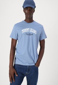 Gaiši zils kokvilnas T-krekls ar uzrakstu "TOMMY JEANS" un "New York" baltā un melnā krāsā. Apvienots ar tumši ziliem džinsiem un atbilstošu cepuri.