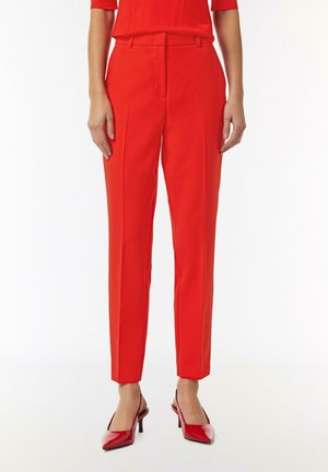 Red tailored trousers with a high waist, slim fit, and front pleats, paired with glossy red pointed-toe heels. Smooth fabric texture.