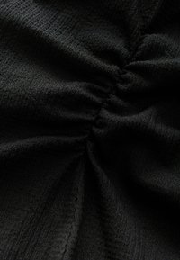 Svart texturerad tyg med draperingsdetaljer, med subtila mönster och en mjuk, skrynklig yta som betonar djup och dimension.