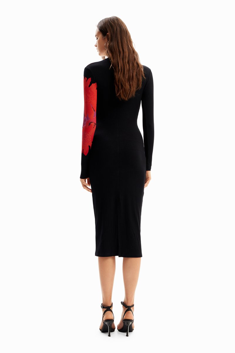 Czarna midi sukienka w prążki z długim rękawem w czerwony kwiatowy wzór i rozcięciem z tyłu. Noszona z czarnymi sandałami na wysokim obcasie.