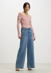 Top rosa chiaro a costine con spalle scoperte e maniche lunghe abbinato a jeans in denim blu a gamba larga a vita alta. Sandali neri con cinturini.