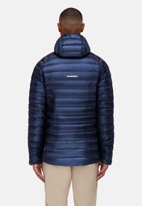 Marineblauwe gewatteerde jas met horizontale stiksels, met een capuchon en logo op de rug. Gladde, glanzende stof met een aansluitend ontwerp.