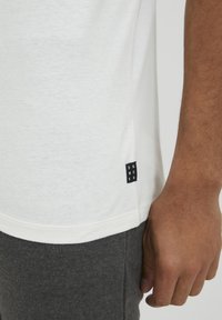 Vit bomull T-shirt med en svart etikett på sidan som visar "DNWOKR". Korta ärmar, rund halsringning, kombinerad med gråa sweatpants.