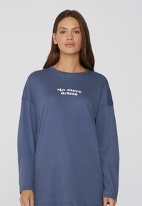 Sudadera de manga larga azul hecha de tela suave, con un cuello redondo y el texto blanco "No más drama" impreso en el centro.
