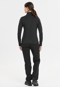 Zwarte lange mouwen top met een hoge kraag, gecombineerd met zwarte broek. De stof lijkt glad en aansluitend, geschikt voor actieve kleding.