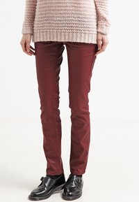 Bordeaux smal passformbyxor med en mjuk textur och framfickor, tillsammans med svarta läderskor. Tröjan är ljusrosa med ett stickat mönster.