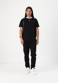 Svart bomulls-t-shirt med vit krage, i kombination med svarta mjukisbyxor. Skorna är vita sneakers, och en svart axelväska bärs på ena axeln.