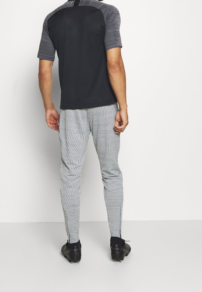 Sportoutfit für Herren mit einem schwarzen T-Shirt mit kurzen Ärmeln und grauen gemusterten, schmal zulaufenden Hosen mit Streifen. Strukturiertes Material; taillierte Passform.