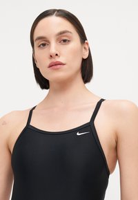 Zwarte bikini met dunne bandjes, gemaakt van glad materiaal. Heeft een klein wit Nike-logo aan de bovenkant aan de linkerkant.