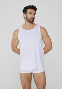 Top sin mangas blanco de algodón con un cuello redondo. La tela es suave y ligera. Se lleva con bragas blancas a juego, mostrando un diseño simple.