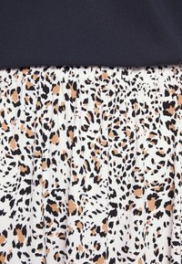 Robe sans manches avec un haut bleu marine et une jupe plissée présentant un fond blanc avec un motif léopard noir et orange.