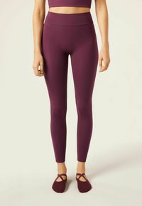 Mörkröda leggings med hög midja, tillverkade av elastiskt material, i kombination med mörkröda balettsockor med korsade remmar.