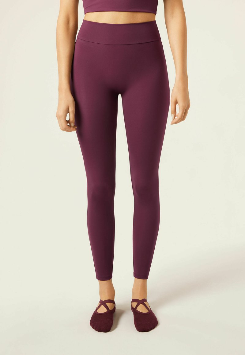 Mörkröda leggings med hög midja, tillverkade av elastiskt material, i kombination med mörkröda balettsockor med korsade remmar.