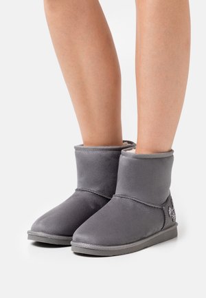 Paire de bottes douces grises mi-mollet avec semelles plates portées sur des jambes nues sur un fond blanc uni.
