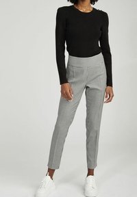 Černý dlouhý rukáv top spárovaný se světle šedými kalhotami s houndstooth vzorem, doplněný bílými teniskami. Hladká textura, přiléhavý střih.