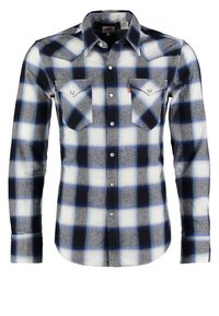 Chemise boutonnée à manches longues avec un motif à carreaux bleu, noir et blanc et deux poches avant à rabat avec boutons.