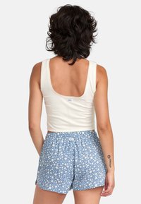 Cream-colored cropped top with a wide scoop back, paired with blue shorts featuring a white floral pattern and elastic waistband.
