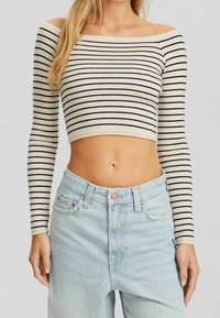 Top corto a rayas sin mangas en crema y negro, con mangas largas y un diseño ajustado, combinado con unos pantalones vaqueros de cintura alta de color azul claro.