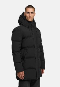 Melnā cepurē ar polsterējumu, ar priekšējo rāvējslēdzēju, elastīgām auklām un sānu kabatām. Audums izskatās gluds un teksturēts.