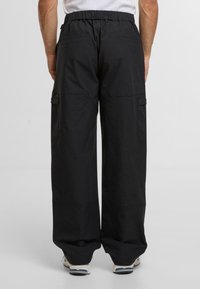 Schwarze Cargo-Hosen mit lockerem Schnitt, elastischem Bund, zwei Gesäßtaschen und Seitentaschen für Funktionalität. Glatte Stofftextur.