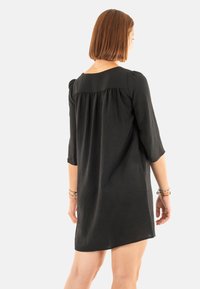 Vestido negro de longitud hasta la rodilla con mangas de tres cuartos, que presenta un diseño de espalda gathered y una tela suave y texturizada.
