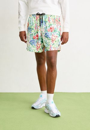 Bloemige zwembroek met een lichte achtergrond en levendige rode, blauwe en groene bloemen, een elastische tailleband en een zwarte trekkoord.