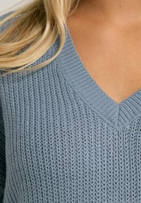 Jasnoniebieski sweter dzianinowy z dekoltem w kształcie litery V, z teksturowanym wzorem i prążkowanymi krawędziami wzdłuż dekoltu.