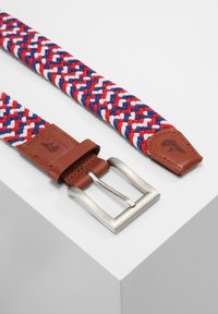 Wykonany z tkaniny warkoczowej w kolorach czerwonym, białym i niebieskim. Brązowy skórzany pasek z metalową, srebrną klamrą oraz wytłoczonym logo na skórze.