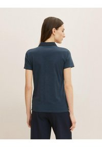 Navy short-sleeve polo shirt with a collar, featuring a smooth texture and a fitted design, paired with dark pants.