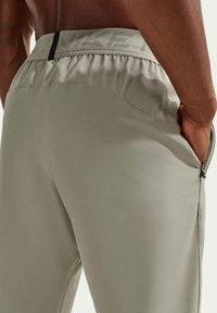 Ανοιχτό γκρι αθλητικό παντελόνι με ελαστική μέση που διαθέτει διακριτικό λογότυπο Nike και τσέπες με φερμουάρ στο πλάι. Λείο, διαπνέον ύφασμα.