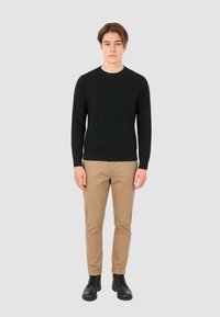Maglione nero a maglia con scollatura rotonda, pantaloni beige e stivali neri con lacci. Design semplice, forma aderente e texture liscia.