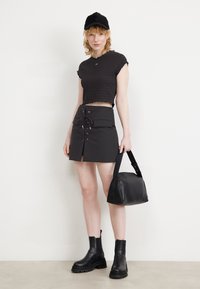 Sort cropped top med smocket tekstur, højttalende sort nederdel med snørebåndsdetalje, sort skuldertaske og sorte chunky ankelstøvler.