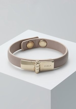 Bransoletka z jasnobeżowej skóry Taupe z pozłacaną klamrą na zawiasach z wygrawerowanym "Furla" oraz dwoma złotymi zatrzaskami do regulacji rozmiaru na białej powierzchni.