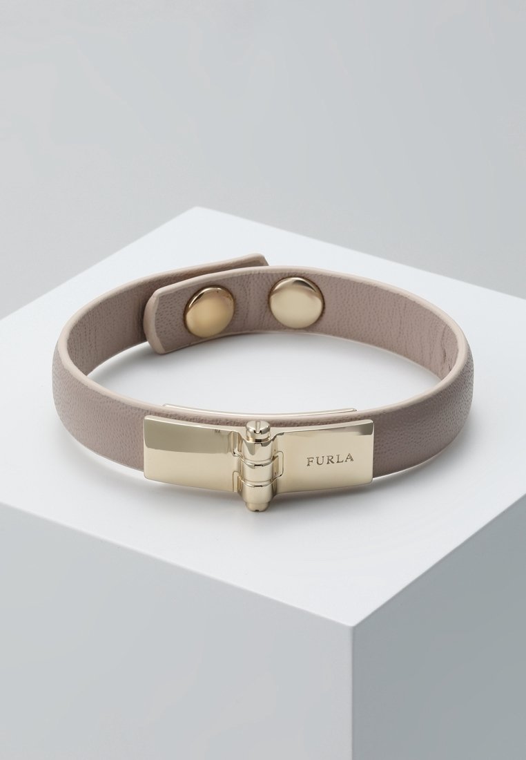 Bracelet en cuir taupe clair avec fermoir à charnière doré gravé "Furla" et deux boutons-pression dorés pour ajuster la taille sur une surface blanche.