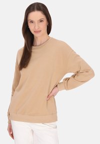 Beige pulóver kerek nyakkal, hosszú ujjakkal és laza fazonnal. A puha anyag sima tapintású, bordázott mandzsettákkal.