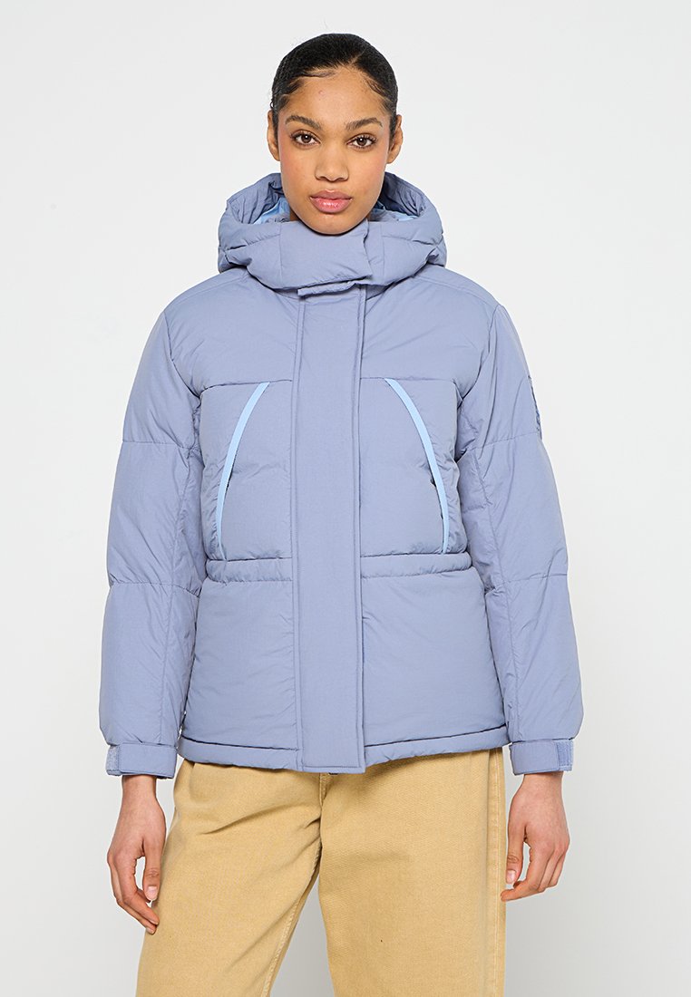 Giubbotto trapuntato azzurro chiaro con collo alto, cappuccio e due tasche laterali con accenti azzurri chiari a contrasto. Texture morbida e trapuntata.