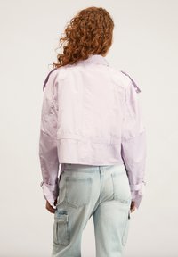 Giacca cropped lavanda con maniche lunghe, dettagli con bottoni e una texture liscia, abbinata a jeans cargo blu chiaro.