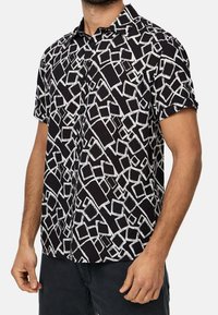 Korte mouwen overhemd in zwarte stof met een wit abstract geometrisch patroon. Gekraagde stijl met knoopsluiting aan de voorkant en een relaxed fit.