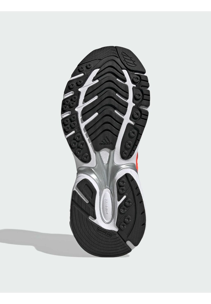 Sort løbesko sål med hvide og sølvfarvede detaljer, der har tekstureret gummitræd, cirkulære grebsmønstre og 'adidas' logo.