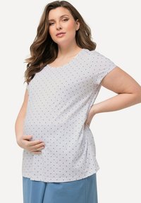 Top de maternidad en algodón blanco con lunares azules, mangas cortas, escote redondo, corte holgado y diseño en capas para mayor comodidad.