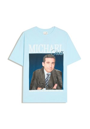 Hellblaues T-Shirt mit einem Foto eines Mannes im Anzug und Krawatte, Text "MICHAEL Scott" und "An office is a place where dreams come true" unten.