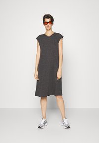 Vestido cinza em algodão de mangas curtas com um corte descontraído, na altura dos joelhos, apresentando um decote redondo e uma textura subtil. Combinado com sapatilhas prateadas.