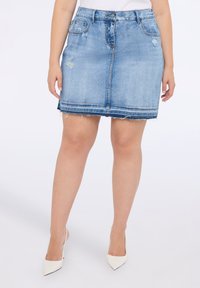 Vaaleansininen farkkuhame, jossa on purjehtiminen helma, etutaskut ja hienovaraiset kuluneet yksityiskohdat, yhdistettynä valkoisiin kärkitossuihin.