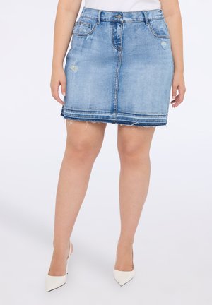 Falda de mezclilla en azul claro con dobladillo deshilachado, bolsillos frontales y detalles sutiles desgastados, combinada con tacones blancos de punta.