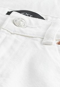 Vita denimjeans har en framträdande silverknapp, platt midjebanddetalj och en svart etikett med varumärkesnamnet.