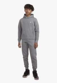 Felpa grigia e pantaloni della tuta realizzati in tessuto morbido, con una tasca frontale e un piccolo logo bianco. Indossati con sneakers nere alte.