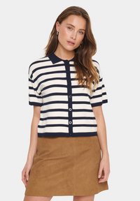 Cardigan a maniche corte, con bottoni, a righe blu navy e bianche, con colletto polo e texture morbida. Abbinato a una gonna marrone.