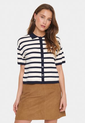 Short-sleeve, button-up cardigan in navy and white stripes, featuring a polo collar and soft texture. Paired with a brown skirt.