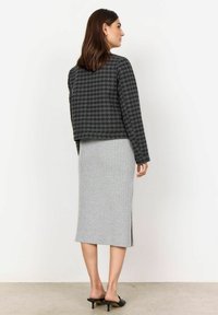 Musta ja harmaa houndstooth-malla cropped-takki, jossa on pitkät hihat, yhdistetty harmaaseen ribbihameeseen, jossa on sivusauma ja mustat korkeat mules-kengät.
