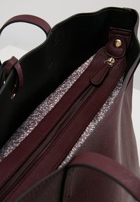 Borsa a tracolla in pelle bordeaux con finitura texture, dotata di un interno nero e di una fodera a motivi floreali, include una tasca con zipper.